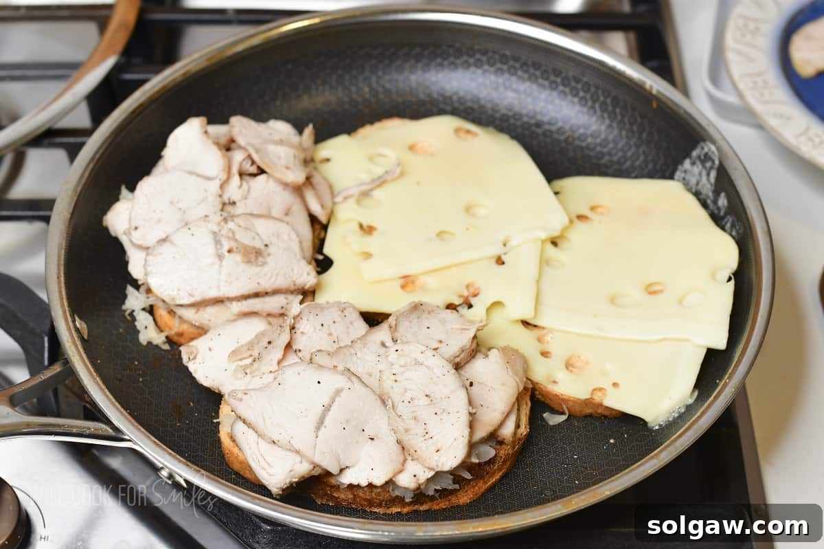 Turkey Reuben Melt 7 Four slices of rye bread in the pan, two with melted Swiss cheese and two with turkey slices layered over the cheese, ready for final assembly.