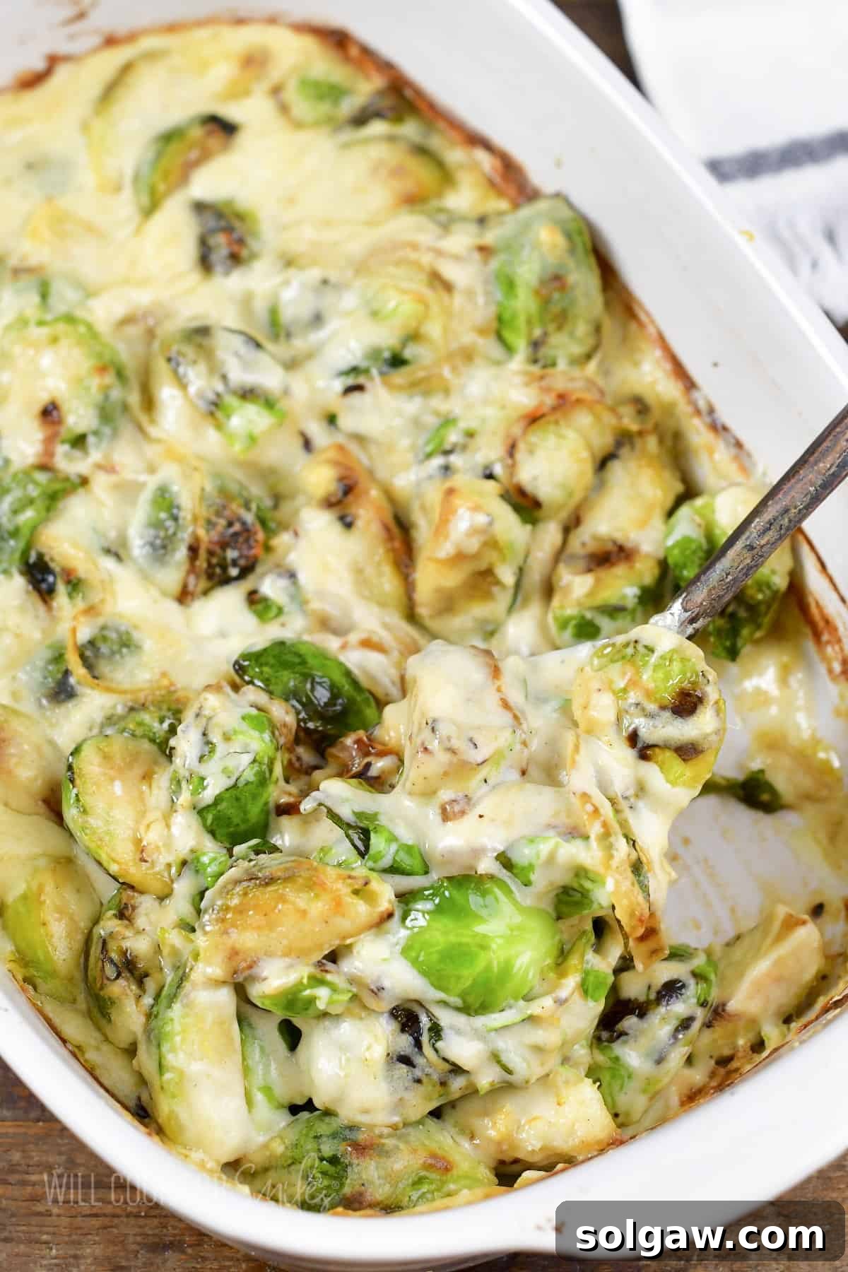 Velvety Baked Brussels Sprouts Gratin 2 scooping out more brussels from white baking dish.