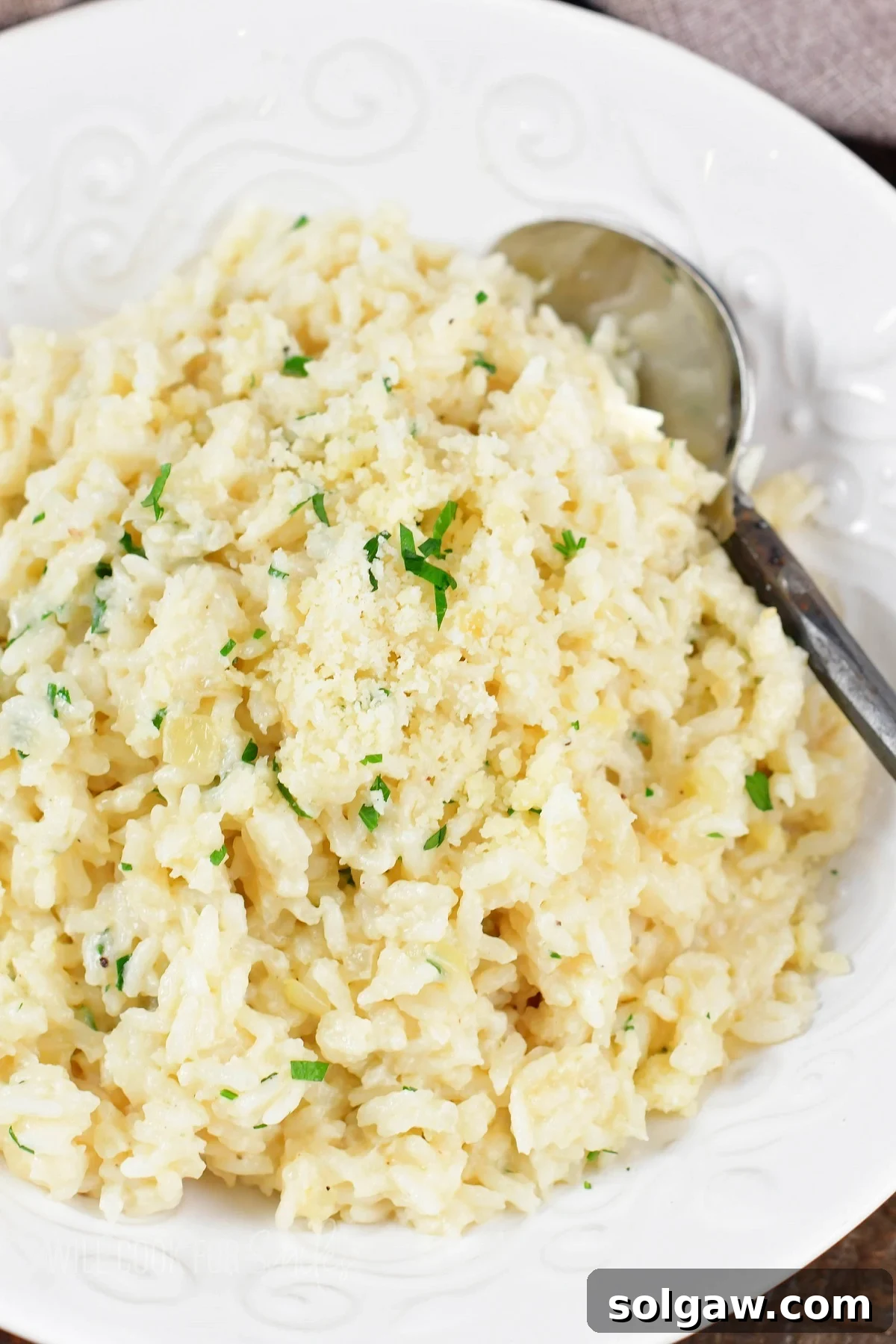 Velvety Parmesan Rice 13 Closeup top view of creamy parmesan rice in a white bowl, garnished with parsley.