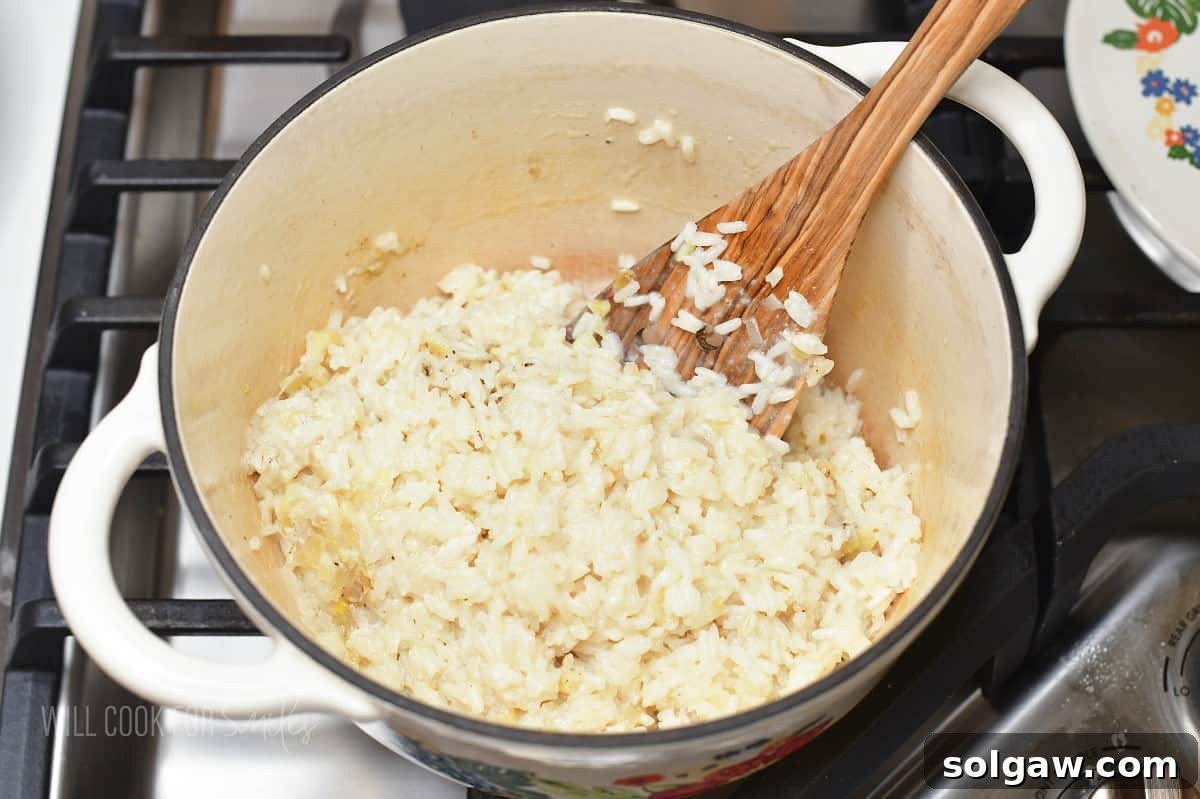 Velvety Parmesan Rice 9 Fluffing cooked creamy rice in a pot with a wooden spatula.