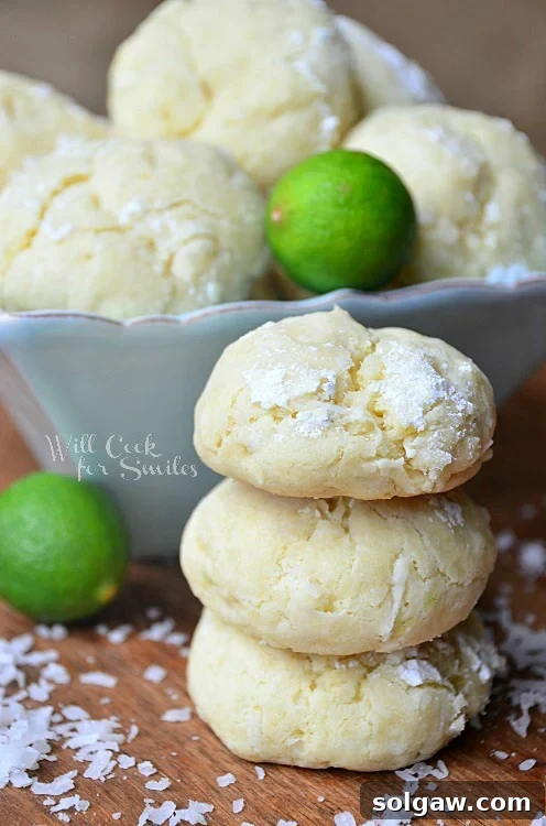 Stack of Chewy Key Lime Coconut Cookies on a rustic wooden table, garnished with coconut shavings.