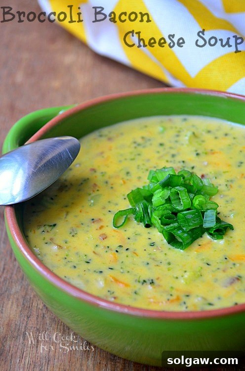 Broccoli soup in a green bowl with green onions sliced on top and a spoon to the left