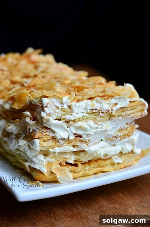 Classic Napoleon Cake 5 A decadent slice of Napoleon Cake on a small white plate, showing the distinct layers and crumb topping, ready to be eaten.