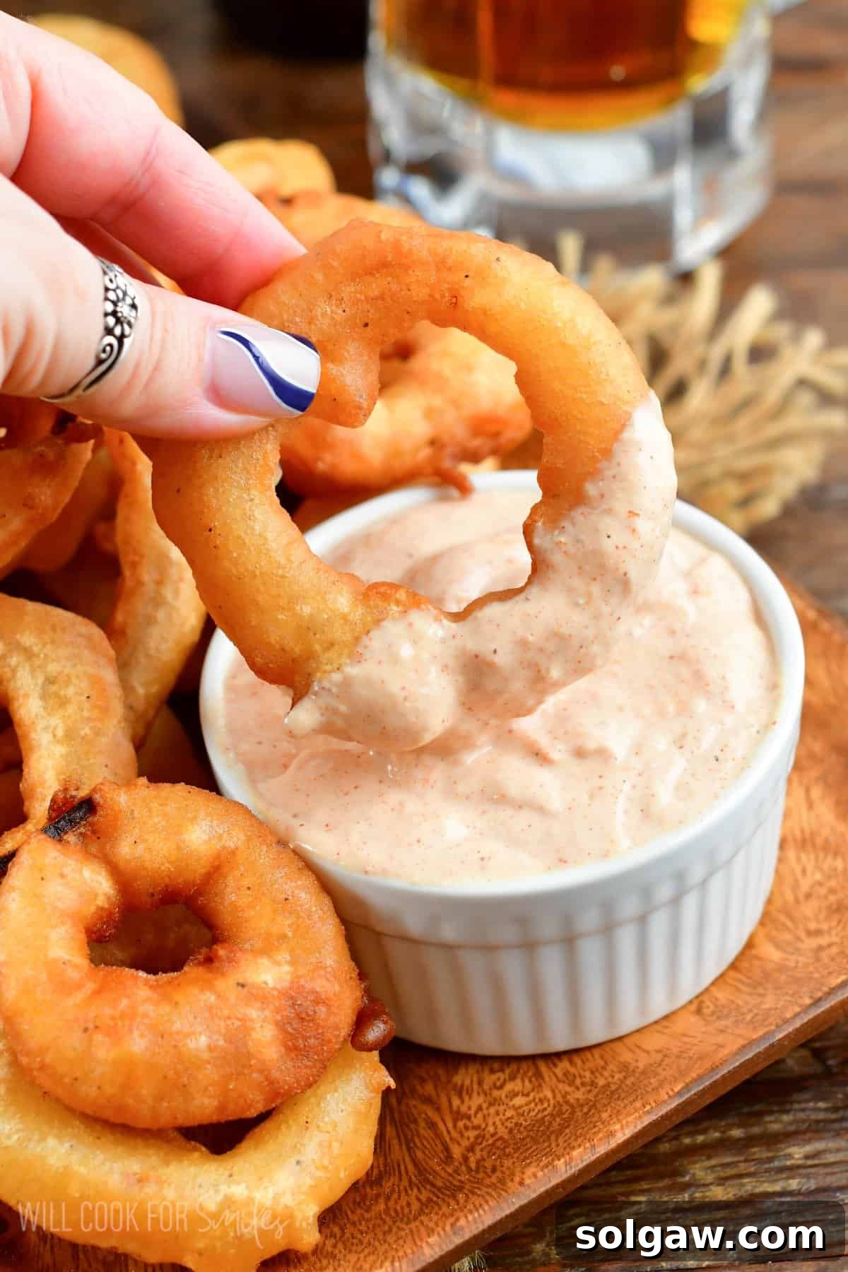 Beer battered onion ring being dopped into sauce that is in a small bowl.