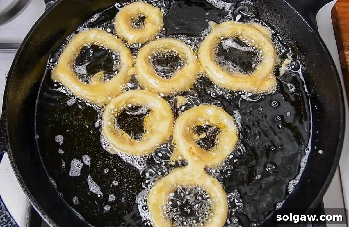 battered onion rings frying in skillet of oil