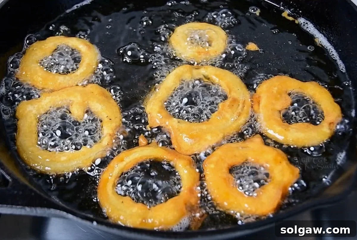 darker color of onion rings frying in skillet of oil