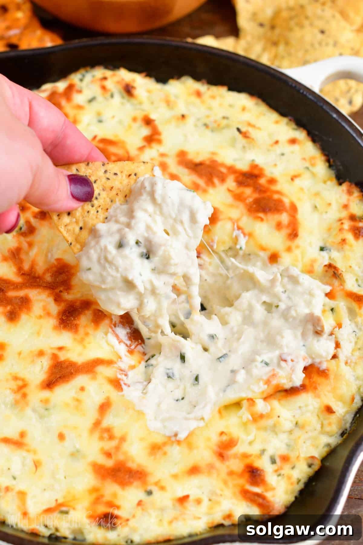 scooping out some creamy chicken dip from the skillet with a tortilla chip.
