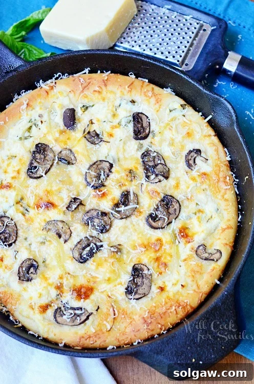 Delicious Asiago Mushroom & Onion White Skillet Pizza in a cast iron pan, surrounded by fresh ingredients and a blue tablecloth, ready to be served