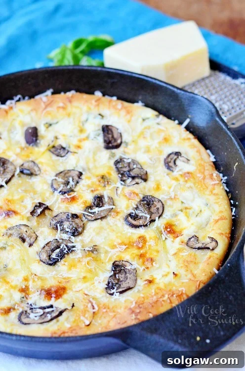 Close-up view of a slice of Asiago Mushroom & Onion White Skillet Pizza being lifted from the cast iron pan, showing the golden crust and melted cheese