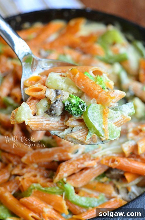 Pasta Primavera in a cast iron skillet with a metal spoon lifting out a creamy portion.