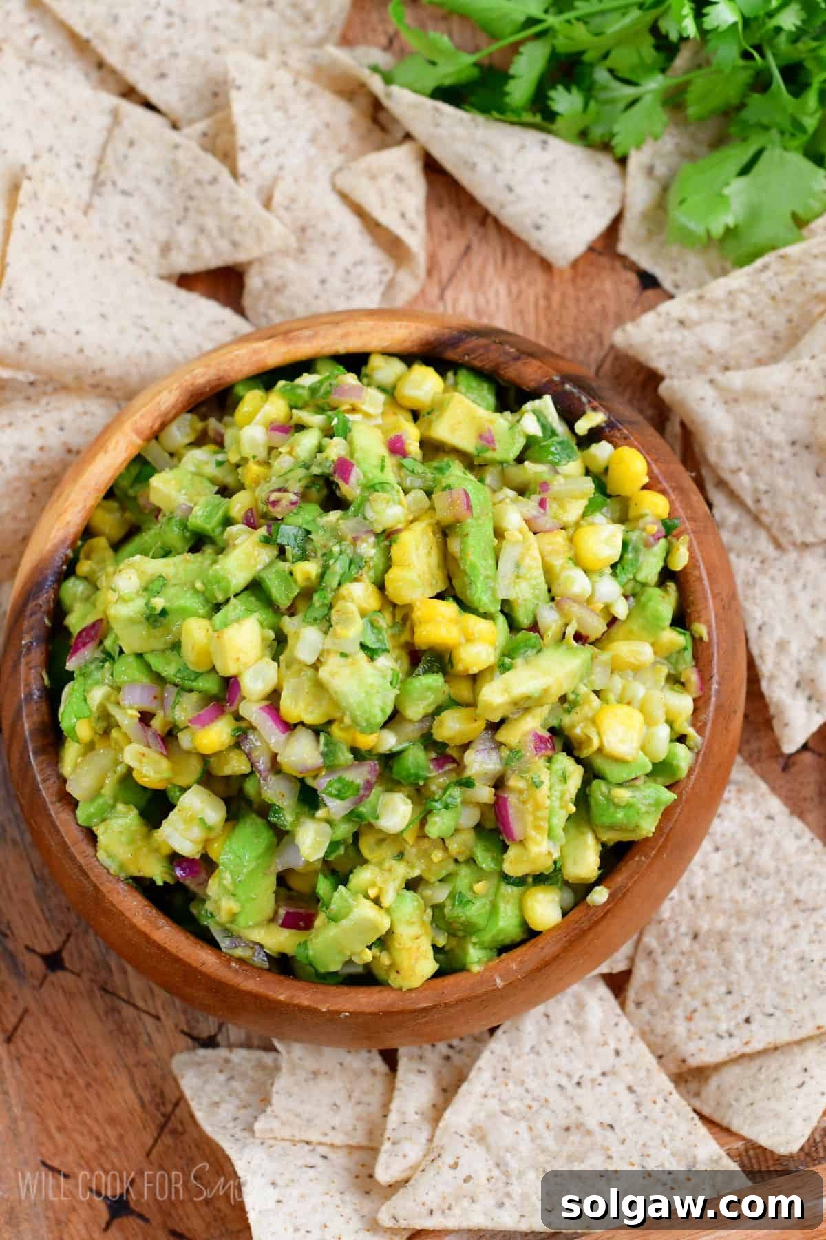 A vibrant bowl of homemade avocado salsa surrounded by crispy tortilla chips, perfect for a summer snack or appetizer.