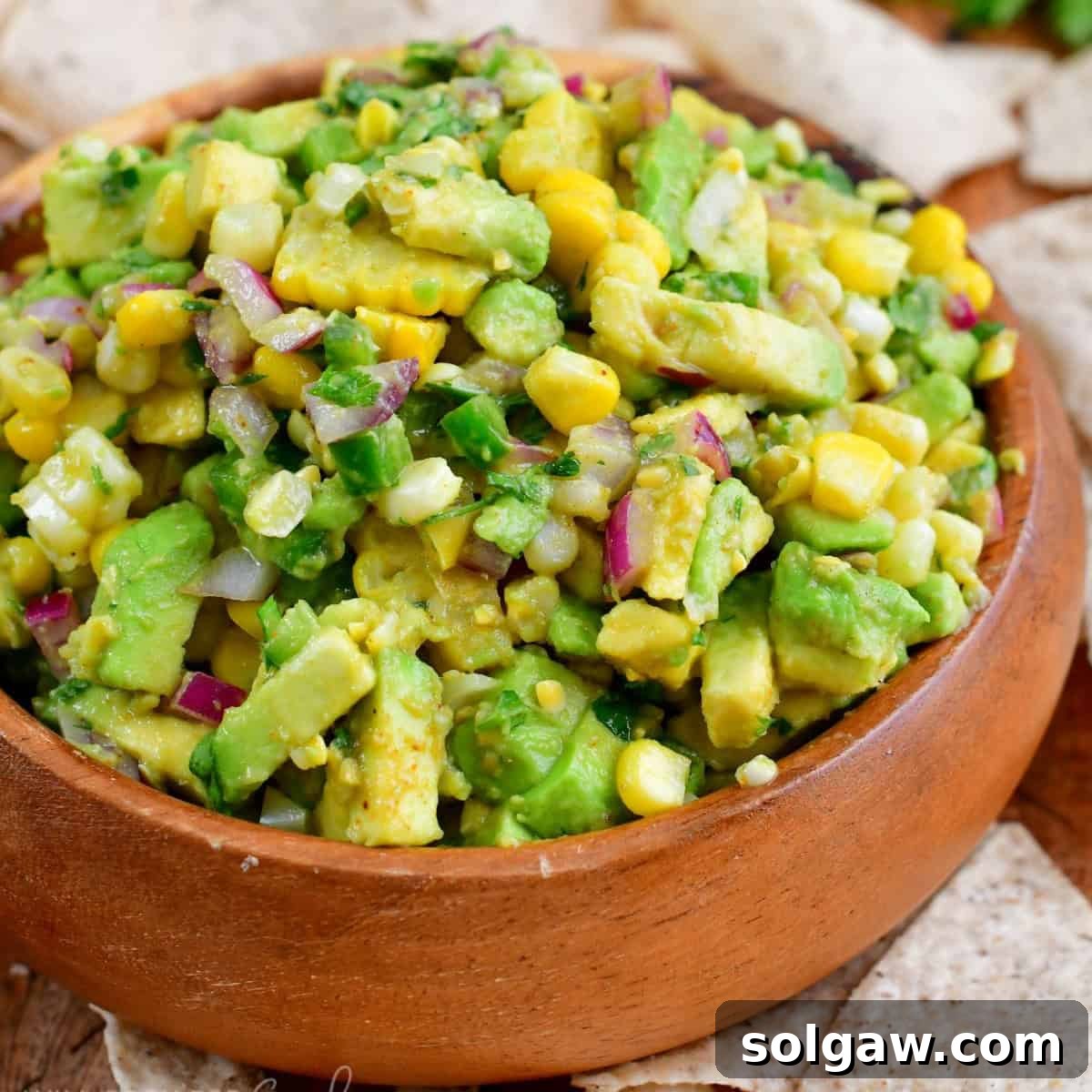 A wooden bowl overflowing with fresh avocado salsa, encircled by golden tortilla chips, inviting a delightful snack experience.