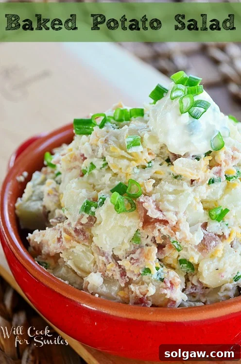 A hearty Baked Potato Salad in a red serving bowl, garnished with sour cream and fresh chives.