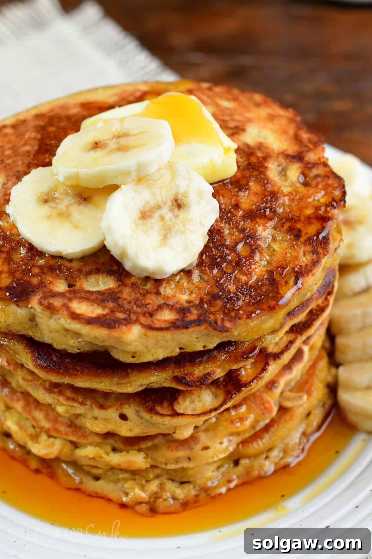 stack of rustic oatmeal pancakes topped with banana slices and butter.