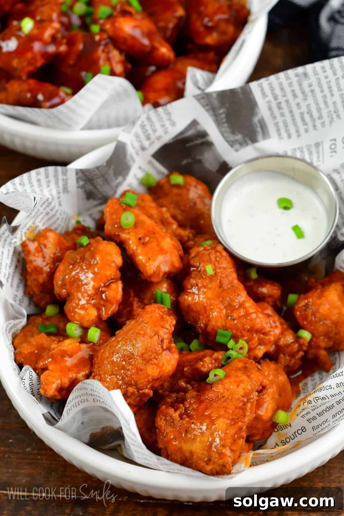 Crispy Chicken Bites 2 buffalo sauce coated boneless chicken wings with green onion on top.