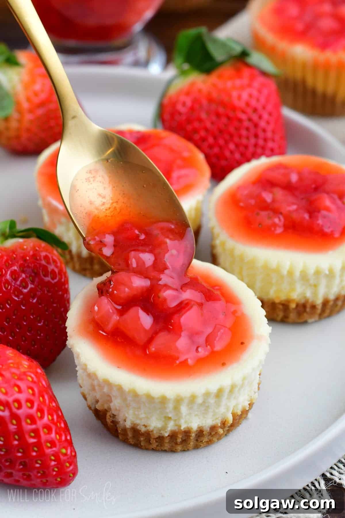 adding some strawberry topping onto a mini NY style cheesecake.