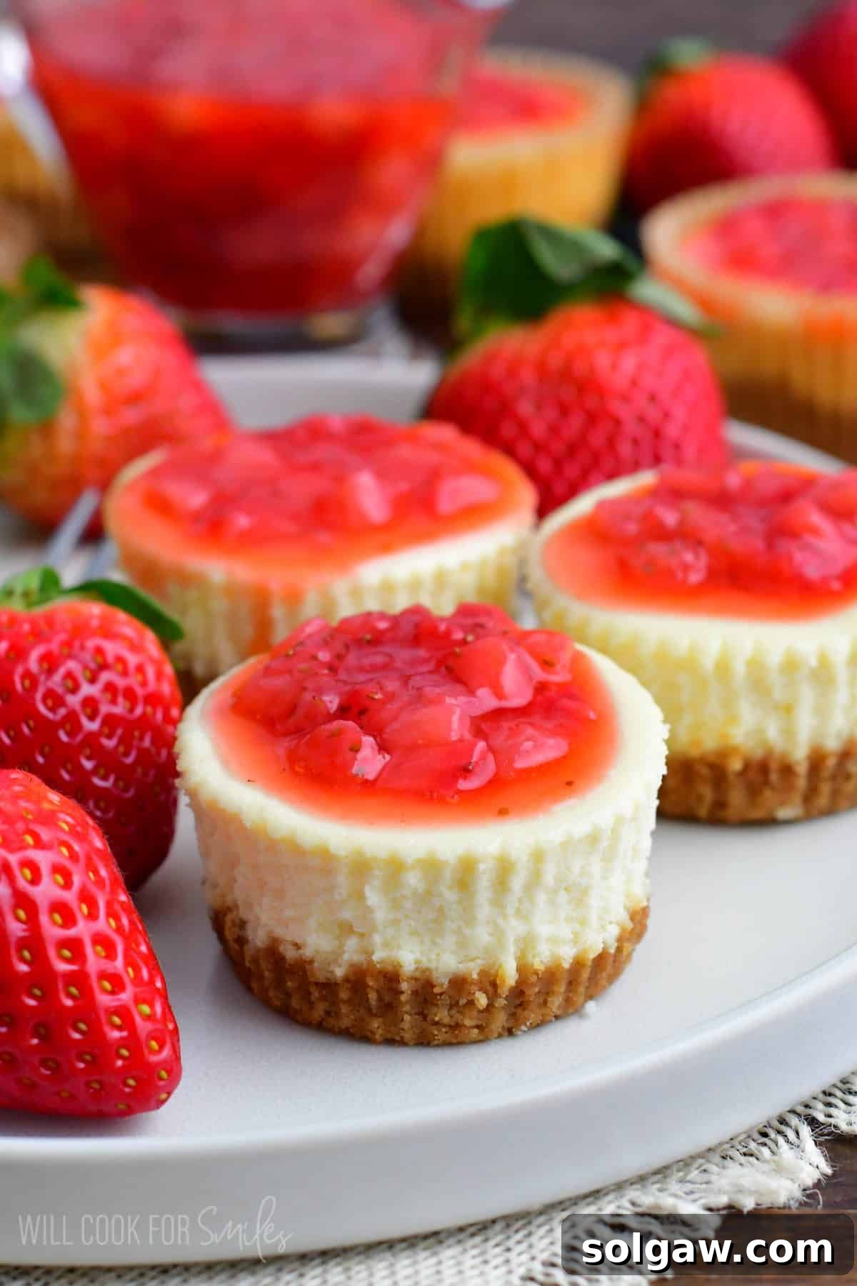three mini cheesecakes on the plate topped with strawberry topping.