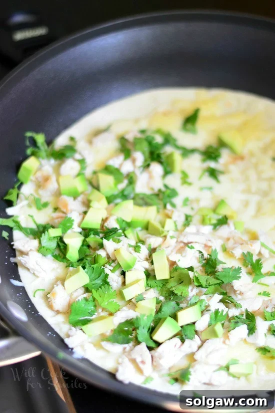 Avocado chicken mixture being placed on a tortilla in a frying pan, illustrating the quesadilla assembly process.