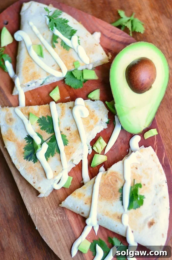 A beautifully presented Avocado Chicken Quesadilla on a cutting board, garnished with fresh cilantro and avocado slices, with a half avocado in the background.