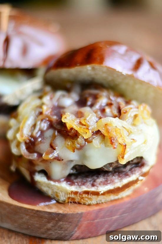 Beautifully presented Buffalo Burger on a pretzel bun with melted cheese, caramelized onions, and demi-glace on a wooden board.