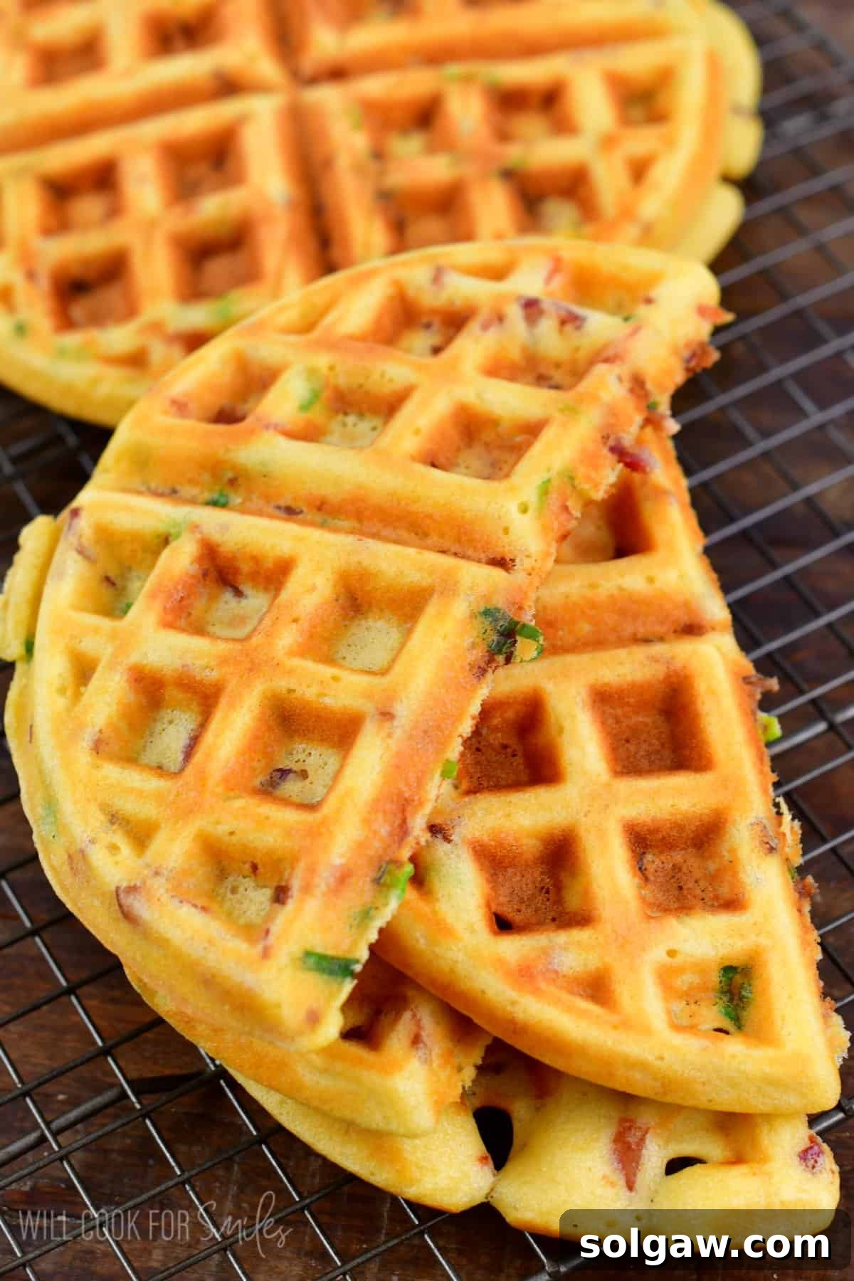 Savory waffles cut in half on wire rack on top of a wood surface, beautifully golden brown and inviting.