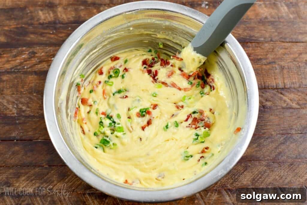 folding ingredients into waffle batter that is in a bowl on a wood surface.