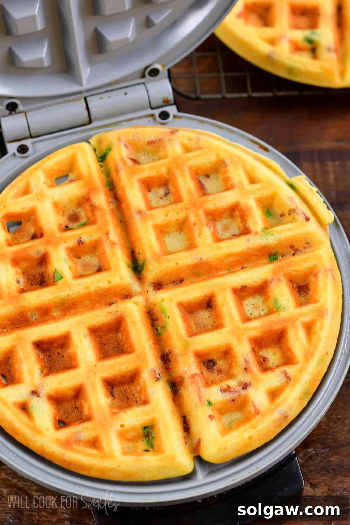 Cooked savory waffles in a waffle maker with the lid open, showcasing their golden-brown texture.