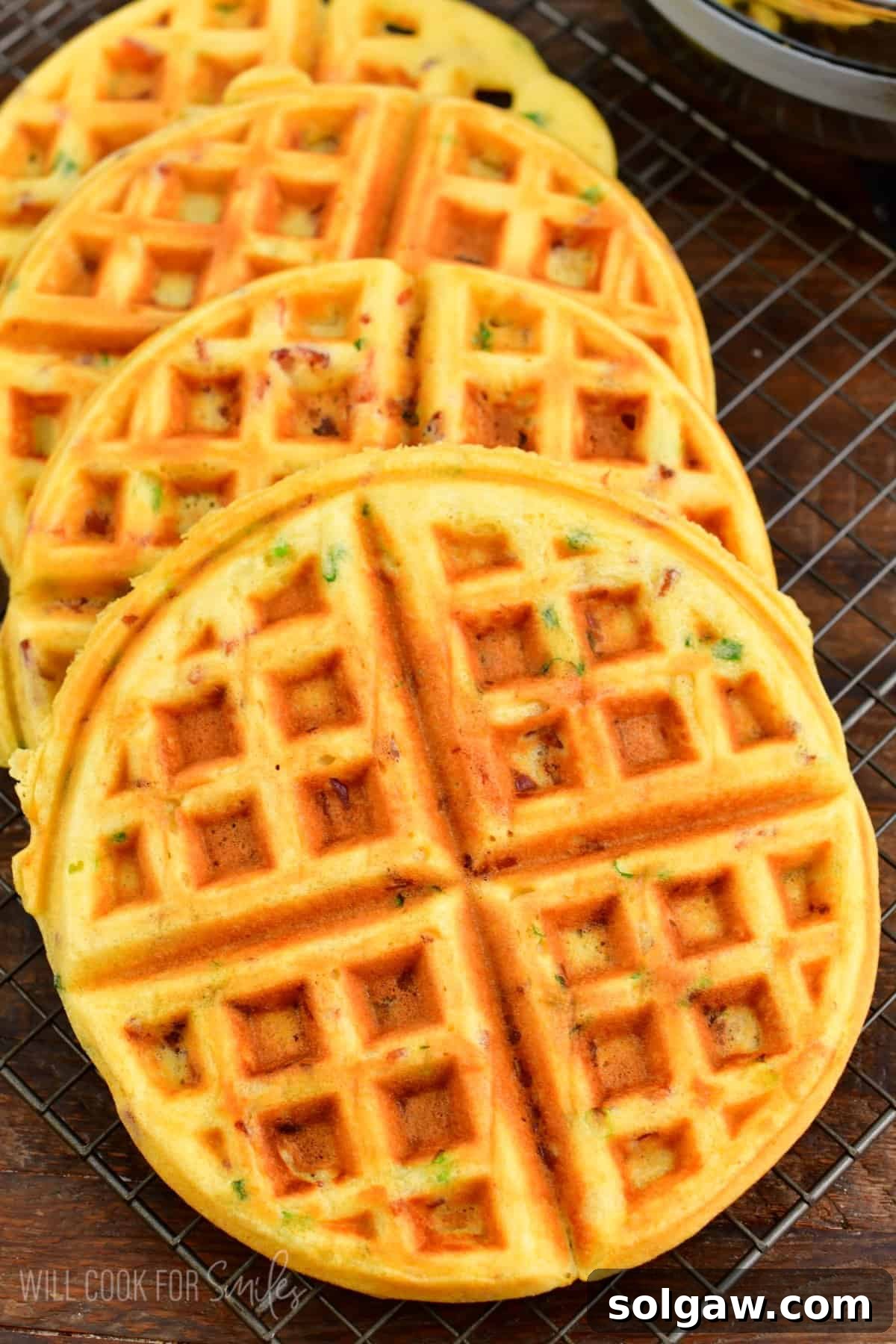 Four cooked savory waffles on a wire rack on a wood surface.