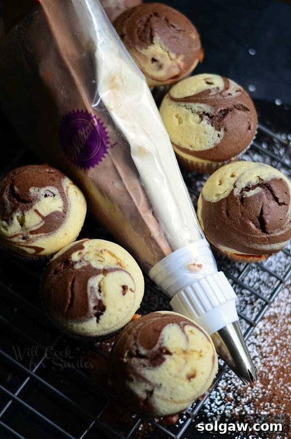 Velvety Marble Cupcakes with Swirled Cream Cheese Frosting 3 Freshly baked Marble Cupcakes cooling on a wire rack, with piping bags filled with chocolate and vanilla frosting resting nearby, ready for decoration.