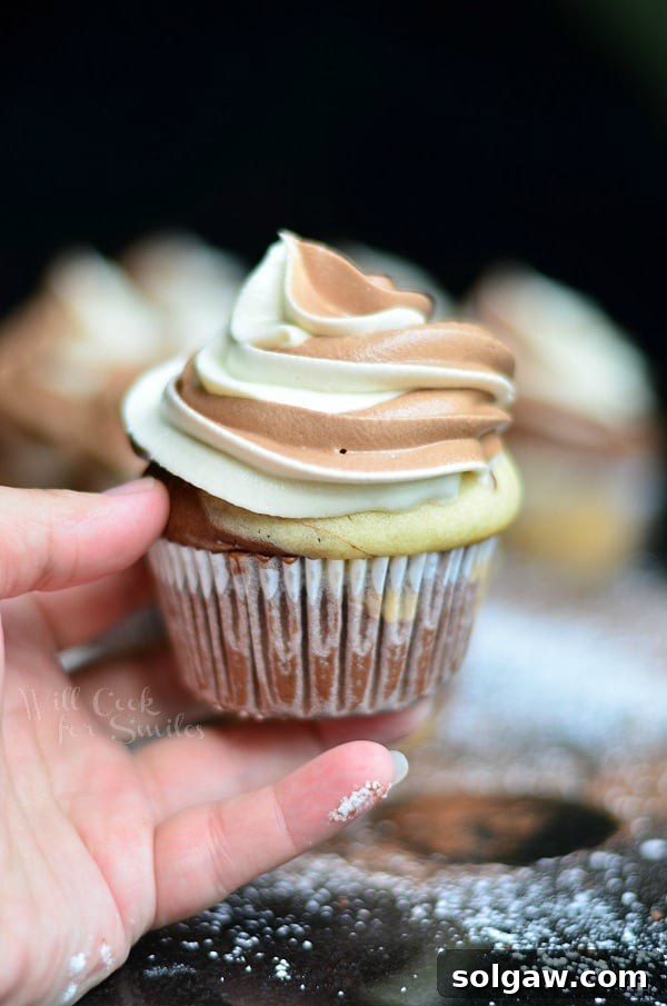 Velvety Marble Cupcakes with Swirled Cream Cheese Frosting 5 A hand holding a beautifully frosted Marble Cupcake, showcasing its delicious appearance and inviting texture.