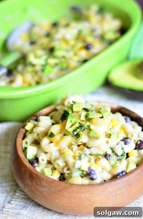 Tex-Mex Mac and Cheese in a wood bowl with avocado on top and the rest of mac and cheese in a green casserole dish