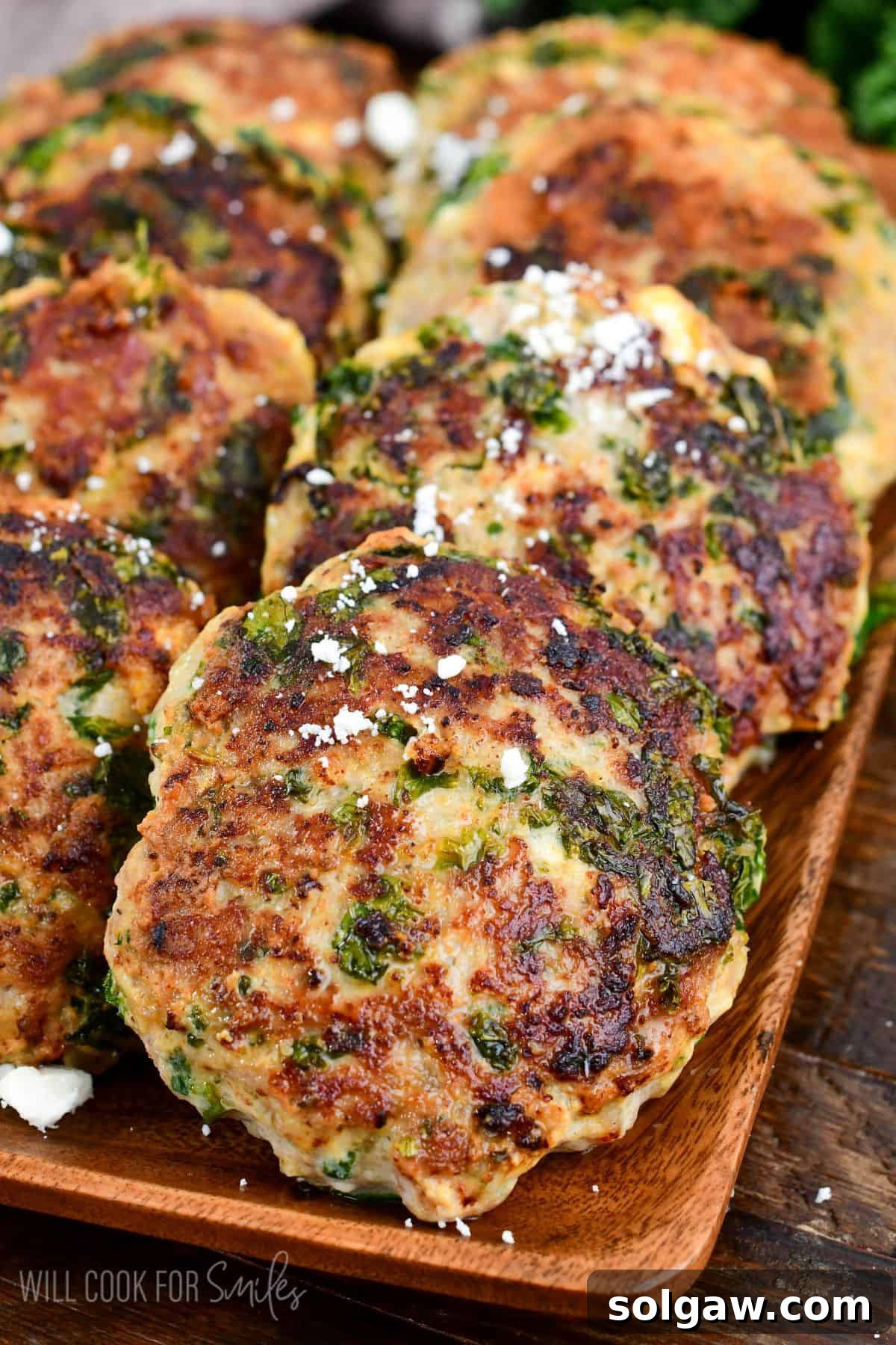 Cooked turkey burgers laid out on a platter, lightly topped with crumbled feta cheese and fresh herbs, ready to be served.