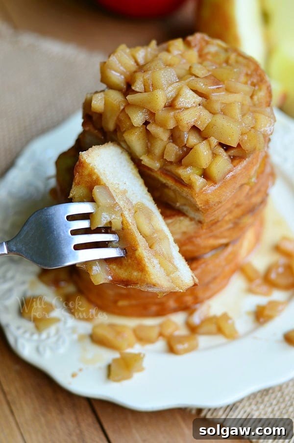 Spiced Apple Pie French Toast 8 A fork taking a bite from a stack of Apple Pie Stuffed French Toast on a plate