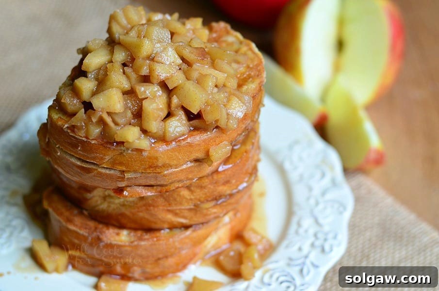 Close up of 3 portions of apple pie stuffed french toast topped with baked apples on white plate
