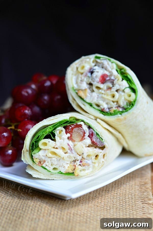 Sweet and Savory Chicken Macaroni 4 A wrap made with chicken salad cut in half and on a white plate with a bunch of grapes.