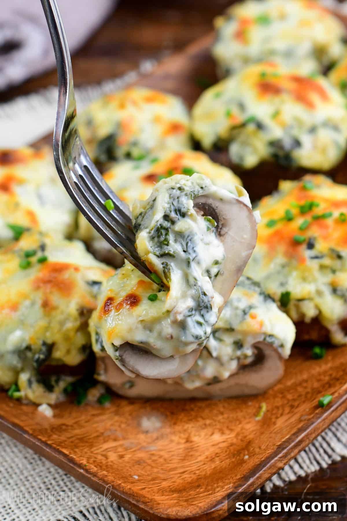 Creamy Spinach Artichoke Stuffed Mushrooms 2 holding sliced mushroom stuffed with creamy spinach artichoke mixture and melted cheese on top.