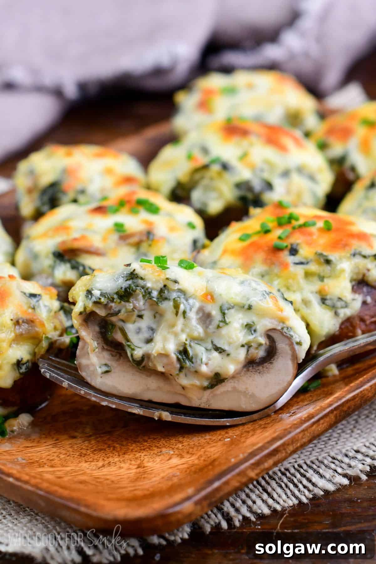 Creamy Spinach Artichoke Stuffed Mushrooms 8 holding half of a creamy and cheesy spinach artichoke stuffed mushroom with melted golden cheese on top.