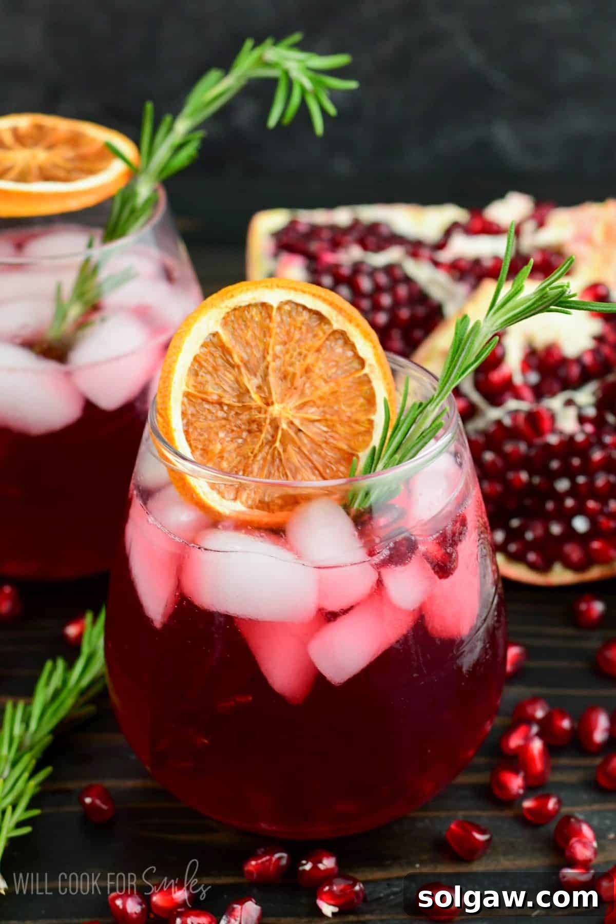 Beautifully deep red pomegranate gin cocktail in a glass garnished with orange and rosemary.