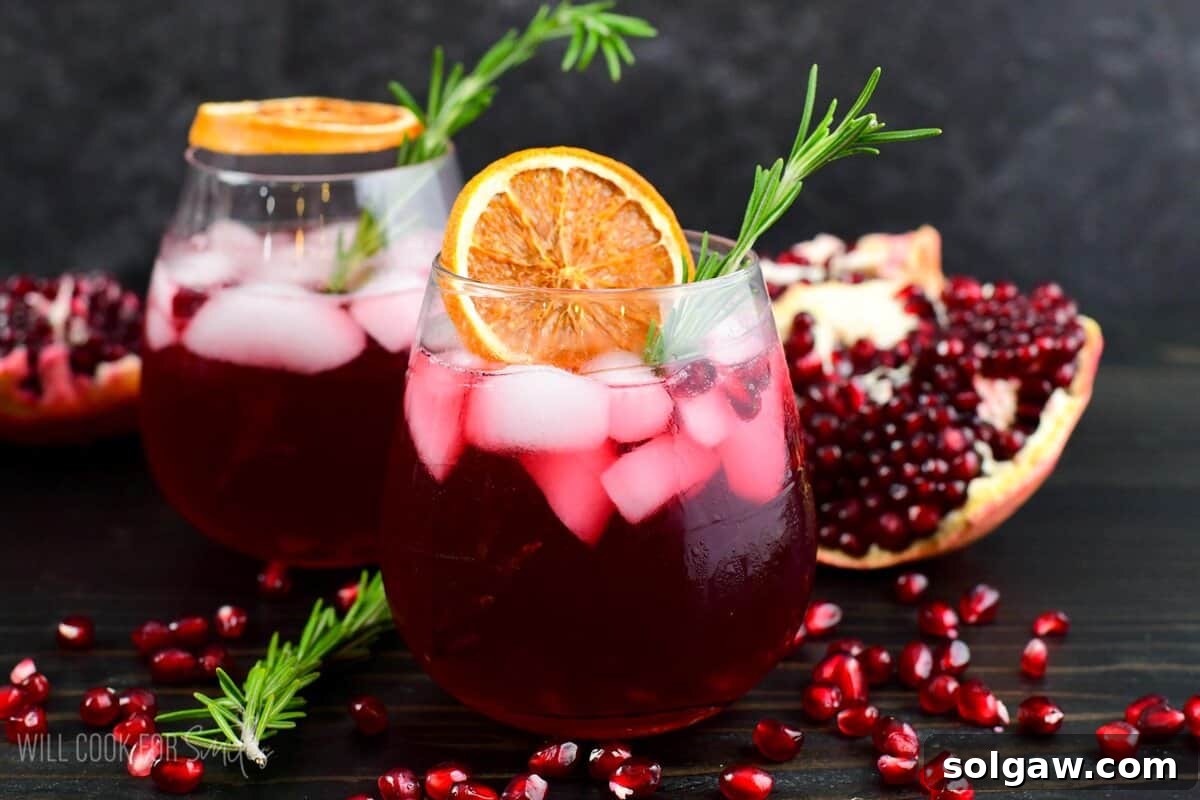 gin cocktail perfect for winter time in a glass with orange and rosemary and pomegranates around.