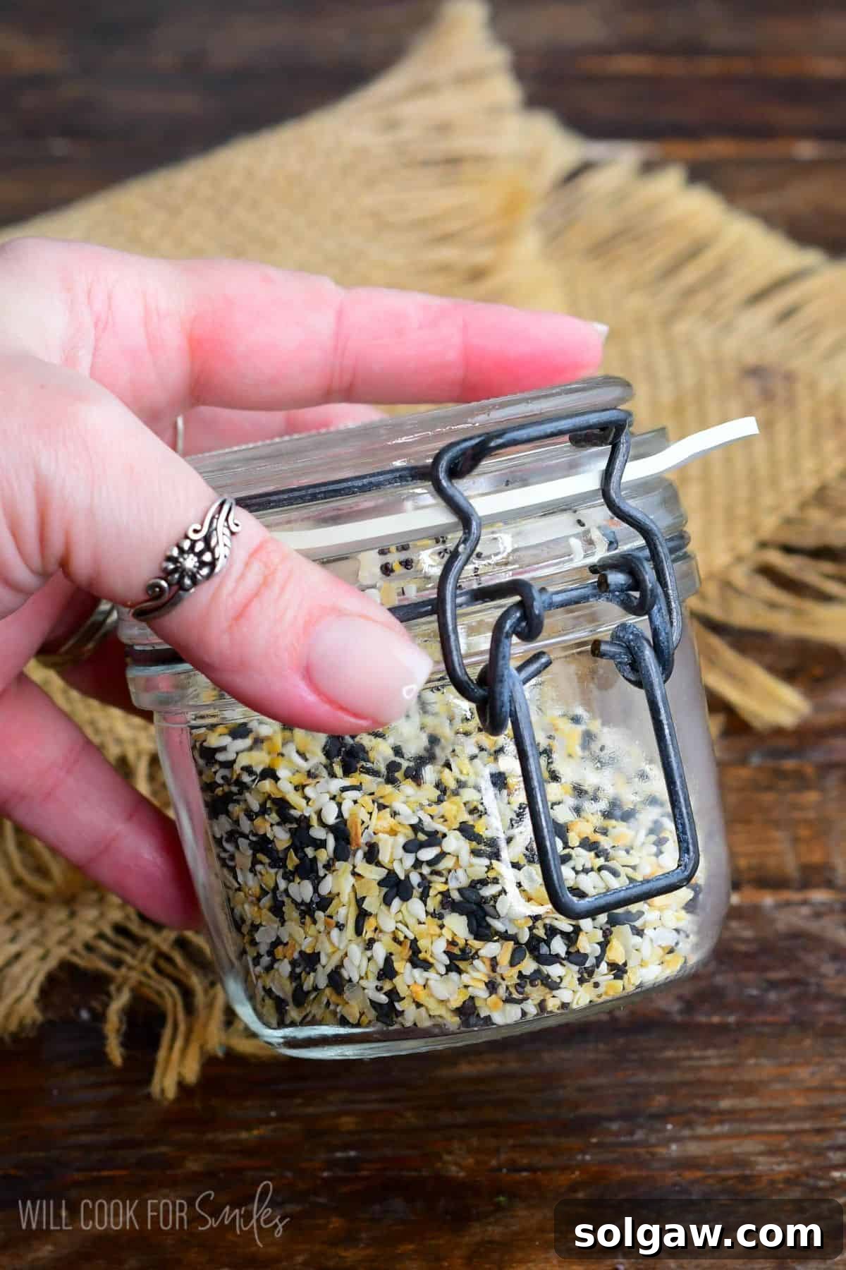 A glass jar filled with Everything Bagel Seasoning being shaken to mix, showing the vibrant blend of ingredients.