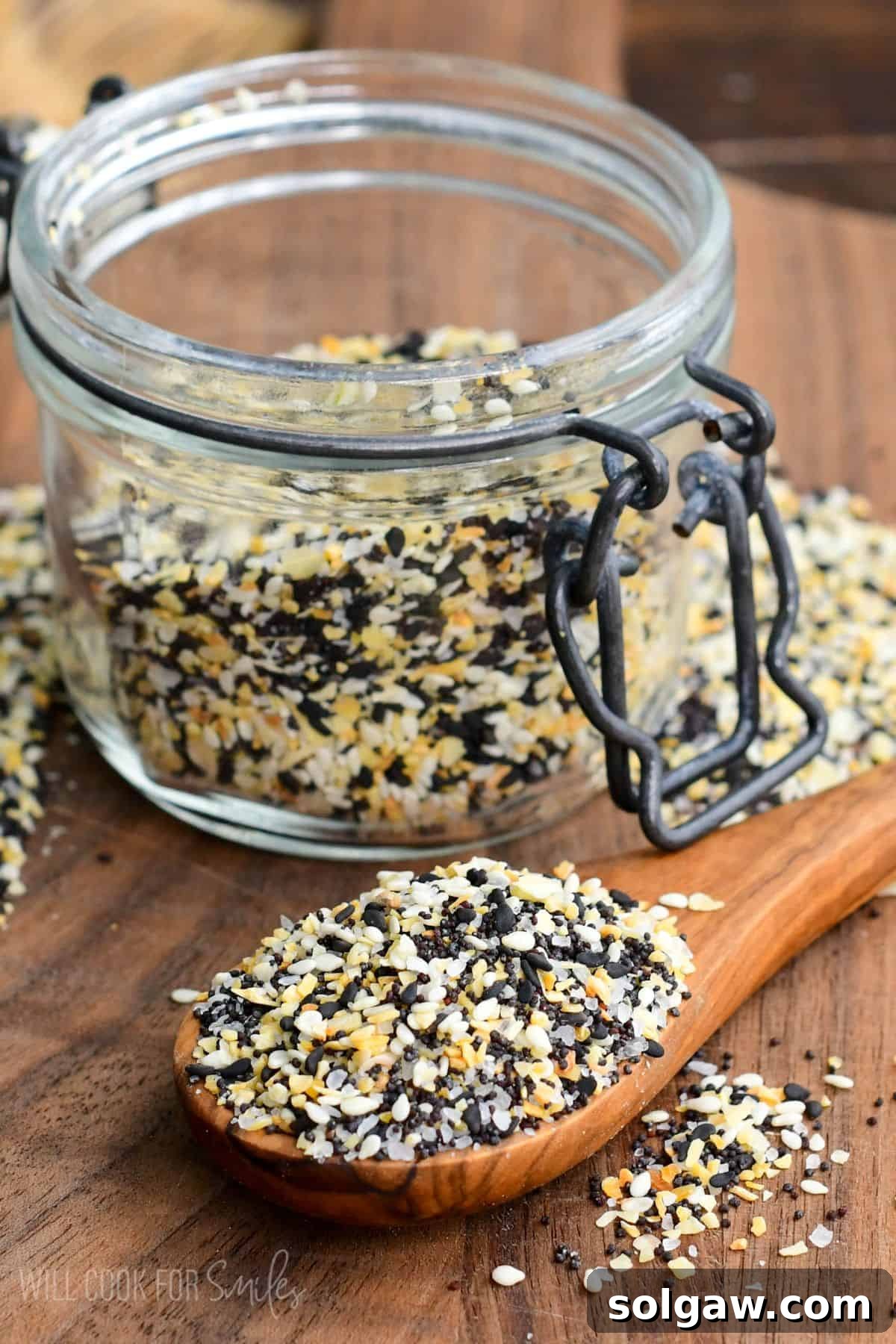 A spoon brimming with Everything Bagel Seasoning next to a glass jar filled with the blend.