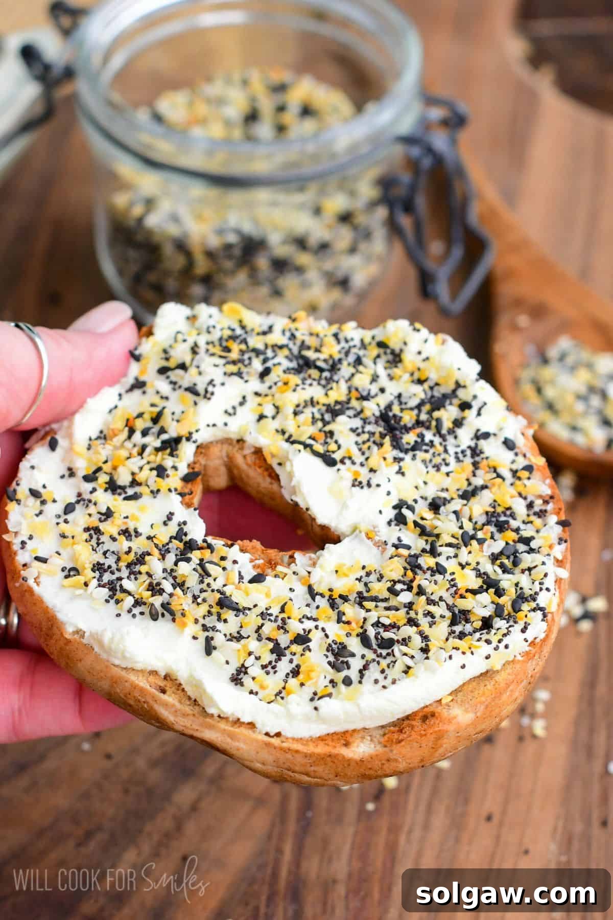 A hand holding a bagel half, generously topped with cream cheese and homemade Everything Bagel Seasoning.