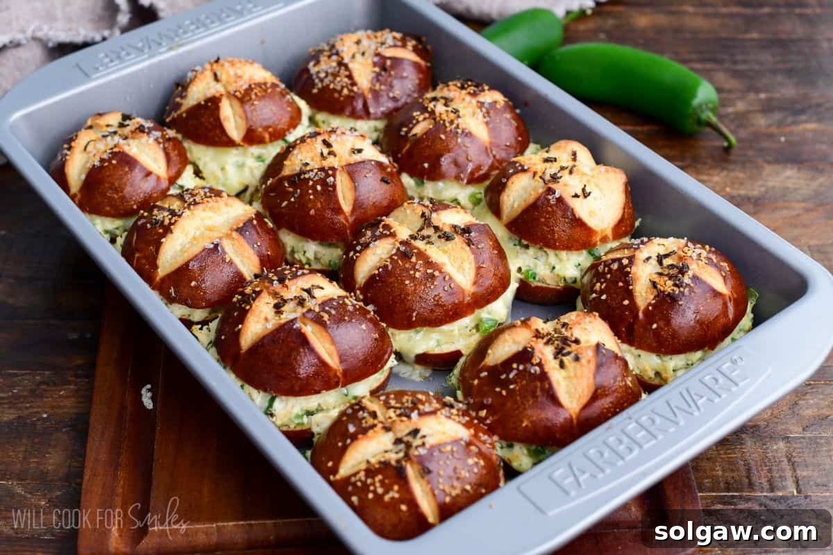 Baked jalapeño ranch chicken sliders on pretzel buns with melted cheese and creamy chicken filling served in a baking pan, ready to be enjoyed.