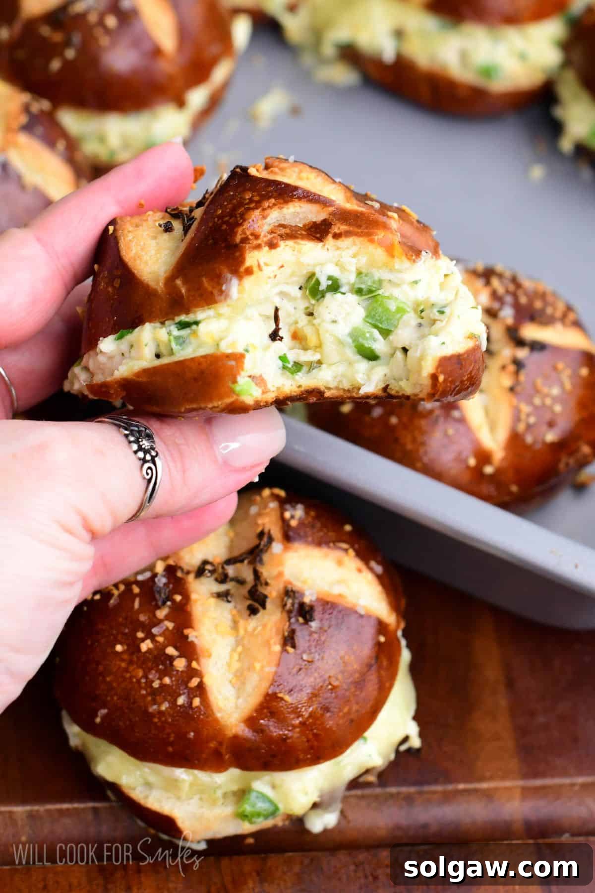 A close-up of a jalapeño ranch chicken slider on a pretzel bun with a bite taken out, showing the creamy chicken and jalapeño filling and melted cheese.