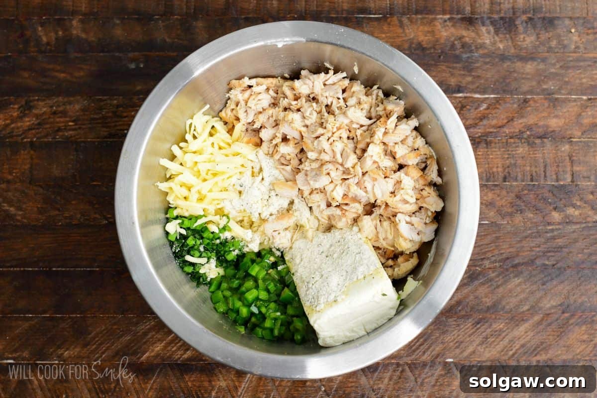 Cooked chicken, cream cheese, Monterey Jack cheese, sautéed jalapeños, herbs, and seasonings added to a mixing bowl.