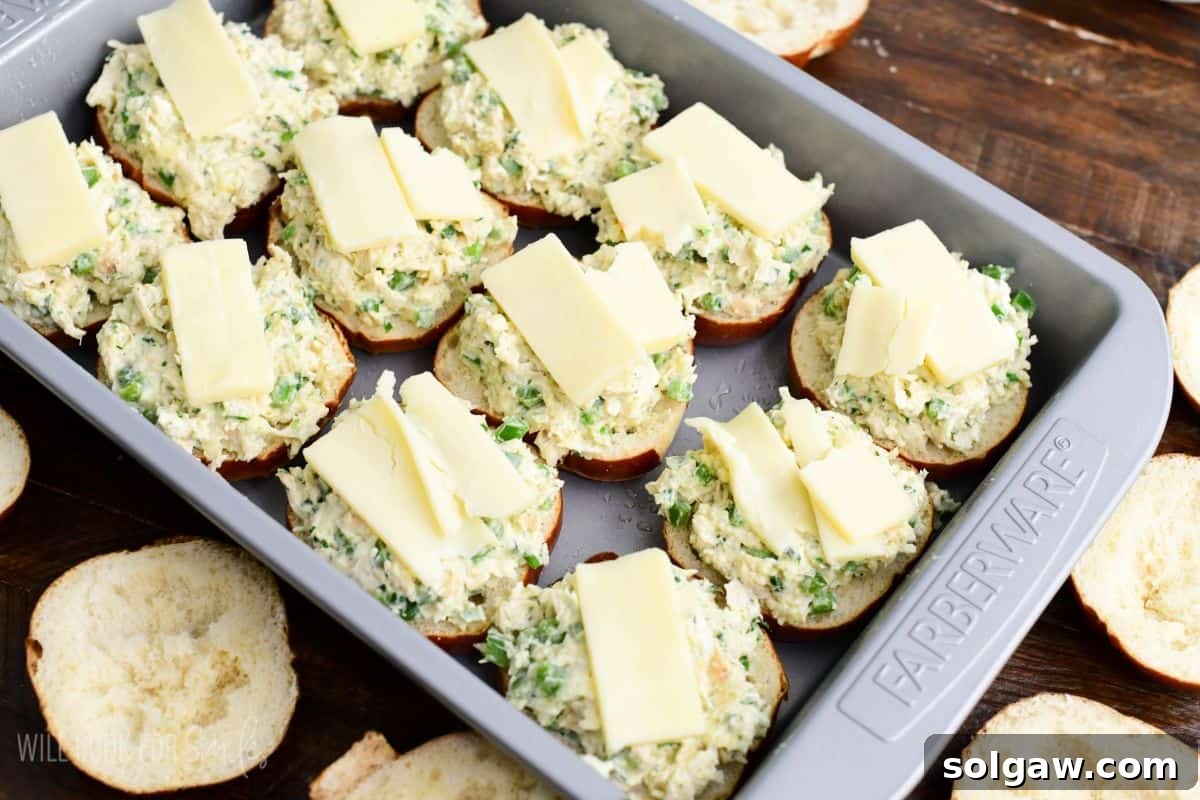 Jalapeño ranch chicken slider buns filled with creamy chicken mixture and topped with sliced cheese before baking, ready for the top buns.