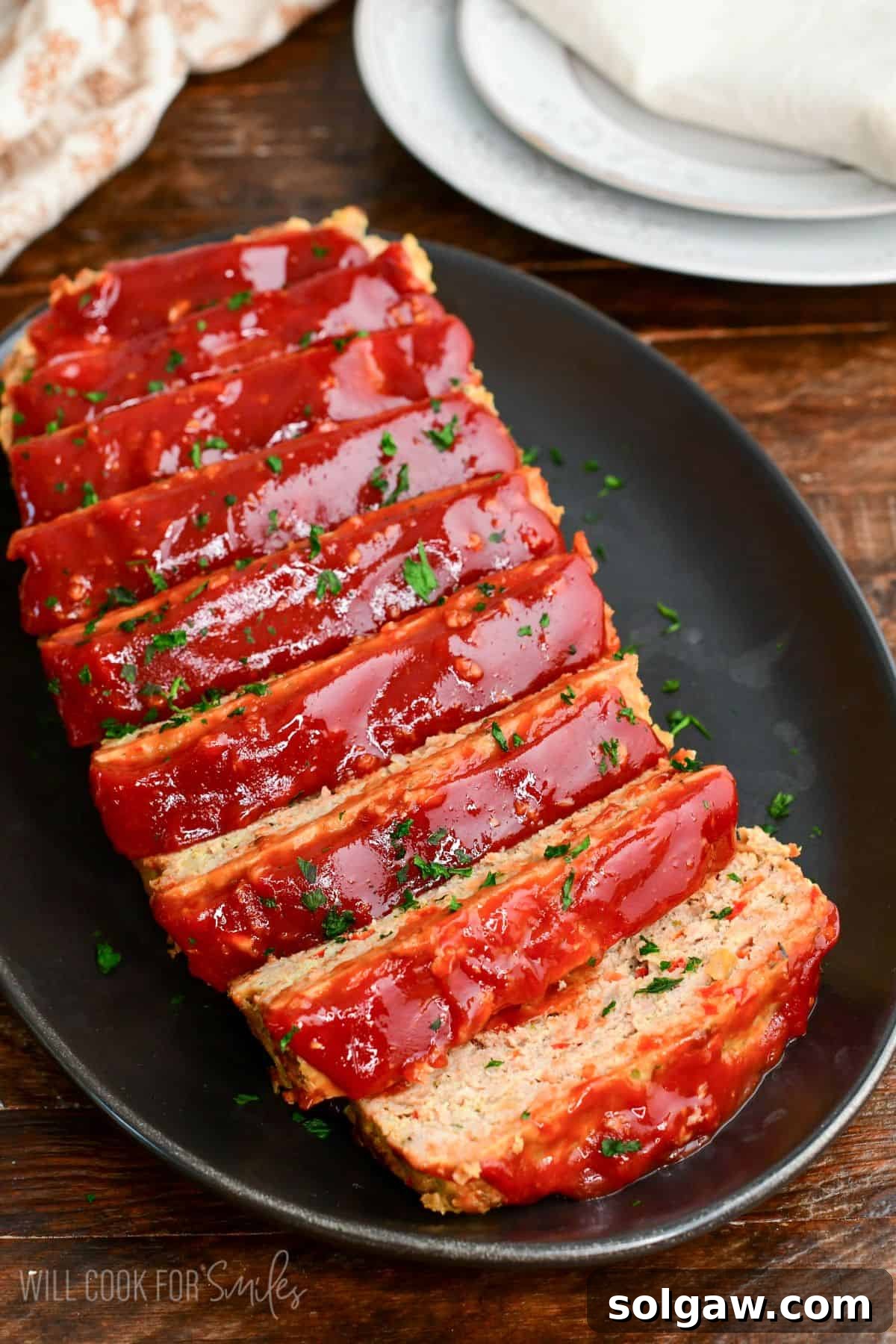 sliced juicy turkey meatloaf with ketchup topping stacked on a black platter. 