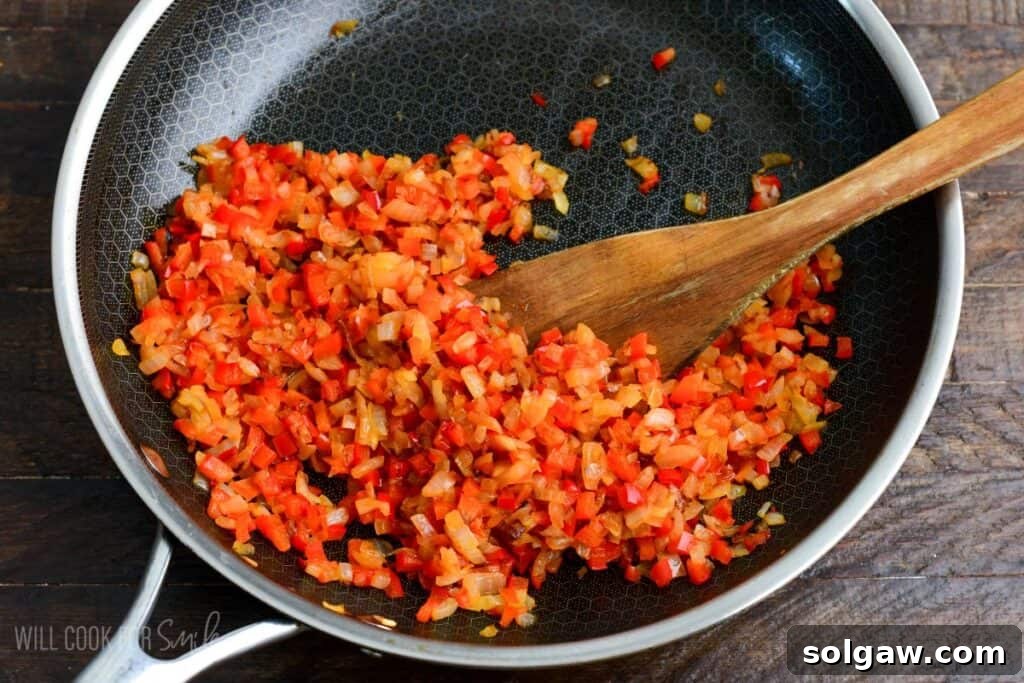 Finely diced red bell peppers and onions sautéing in a skillet with a wooden spoon, cooking down for turkey meatloaf.