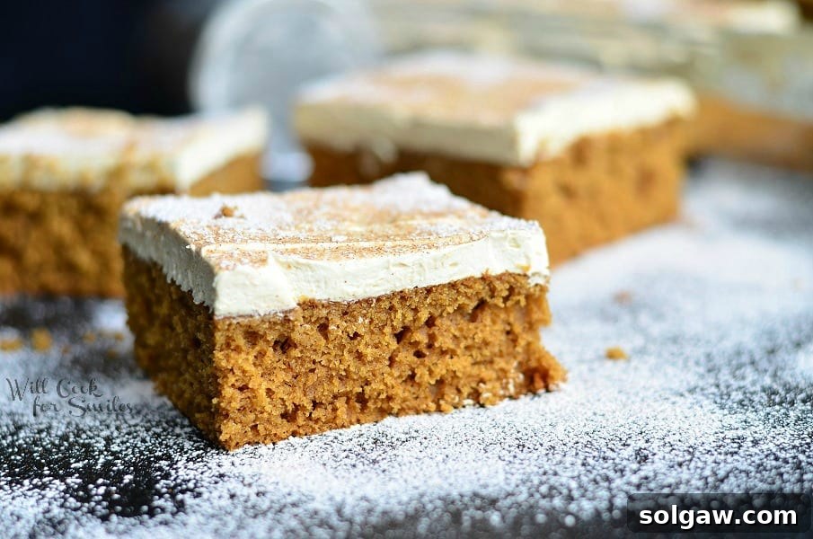 Large slice of gingerbread cake with frosting and maple drizzle on a rustic wooden table.