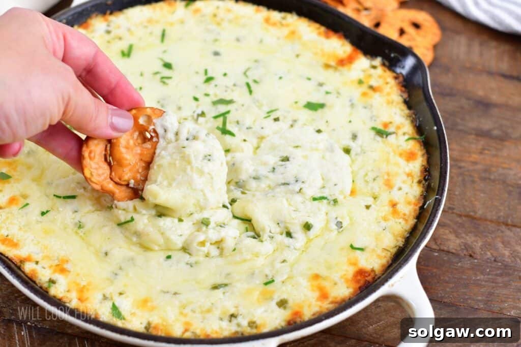 closeup of scooping hot cheese dip with a pretzel chip, showing its irresistible texture.